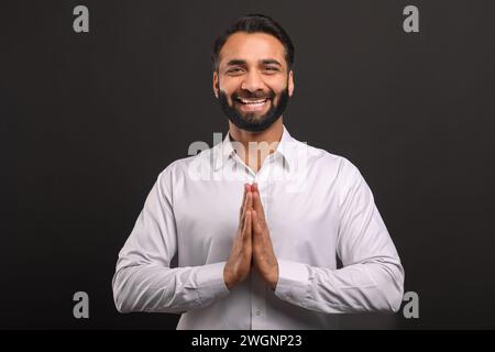Mit Händen zusammen in einer Geste der Dankbarkeit oder Begrüßung schlägt der Geschäftsmann eine einladende Unternehmenskultur vor. Konzept einer Mischung aus traditionellem Respekt und zeitgenössischen Geschäftspraktiken Stockfoto