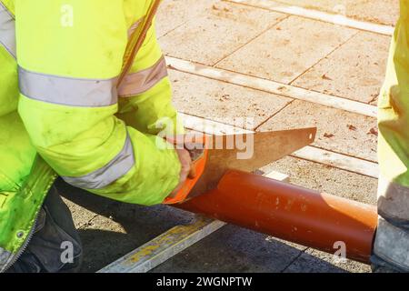 Bauherr schneidet Kunststoffrohre mit Handsäge während der Konstruktion des internen und externen Abflusssystems des neuen Hauses Stockfoto