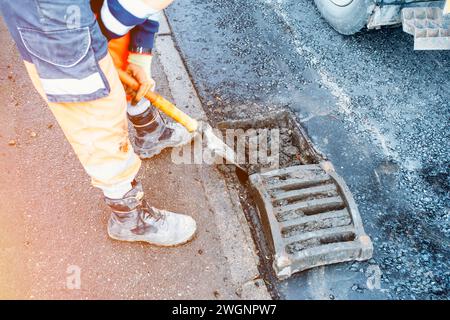 Bauherr reinigt blockierte Straßenrinnen mit Schaufel und Vakuumbagger Stockfoto