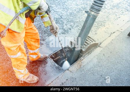 Bauherr reinigt blockierte Straßenrinnen mit Schaufel und Vakuumbagger Stockfoto