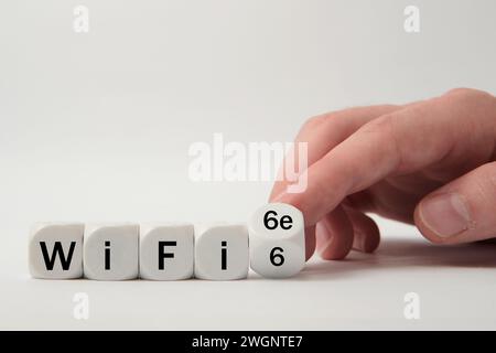 Die Hand würfelt und ändert den Ausdruck „WiFi 6" auf „WiFi 6e“ auf weißem Hintergrund Stockfoto