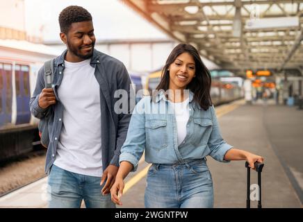 Ein junges Familienpaar läuft entlang des Bahnsteigs, um den Zug zu nehmen, um in Urlaub zu fahren Stockfoto