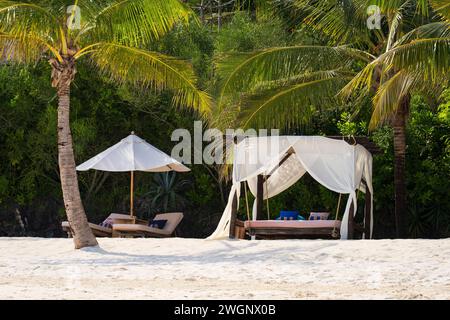 Weiße Stranddächer und Sonnenschirm bei Sonnenuntergang. Luxuriöse Strandzelte im luxuriösen Strandresort. Sommer-Strandkonzept, unbeschwert, Erholung am Meer, Niemand auf Stockfoto