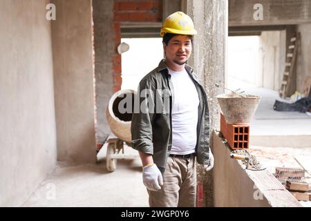 Lächelnder junger Maurer an unvollständiger Wand Stockfoto