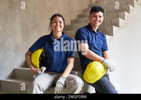 Lächelnde junge Kollegen, die auf unvollständiger Treppe sitzen Stockfoto