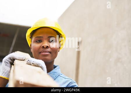 Selbstbewusste Schreinerin, die Planken auf der Schulter trägt Stockfoto