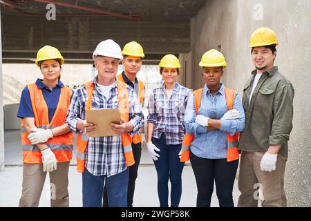 Selbstbewusster männlicher Baumeister mit Team, das Schutzhelme trägt Stockfoto