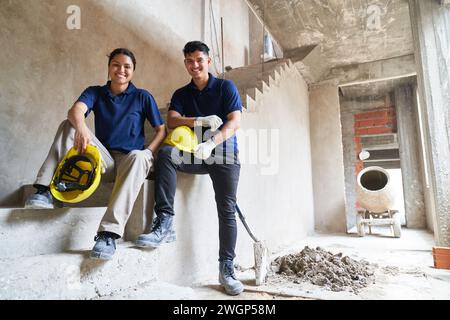 Lächelnde junge Maurer sitzen auf unvollständiger Treppe Stockfoto