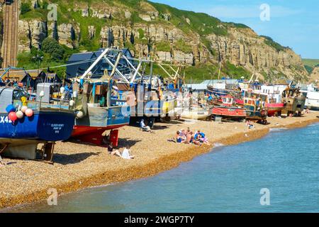 Menschen, die sich am Strand von Hastings Fishing Boat Beach in Est Sussex, Großbritannien, sonnen Stockfoto