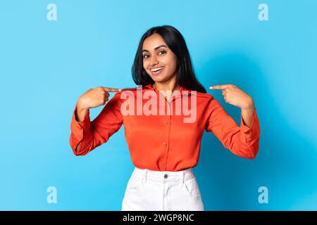 Glückliche junge indianerin, die mit den Fingern auf sich zeigt, blauer Hintergrund Stockfoto