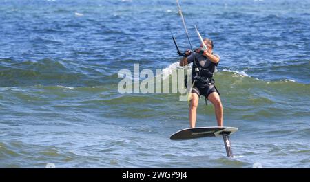 Gilgo Beach, New York, USA - 13. August 2023: Seitenansicht eines Mannes, der einen Drachen hält, während er im Atlantik vor der Küste von Lont Island New Yo surft Stockfoto