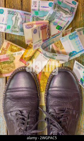 Die Beine eines Mannes in schwarzen Schuhen stehen auf russischem Papiergeld, verstreut auf dem Boden, von oben Stockfoto