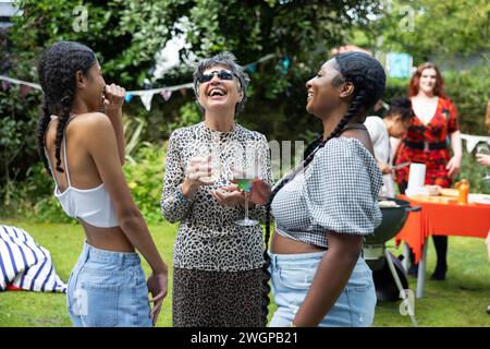 Ältere Frau lacht und hat Spaß mit zwei jungen Frauen / Enkeltöchtern / weiblichen Freunden auf einer Sommer Garten BBQ Party. Stockfoto
