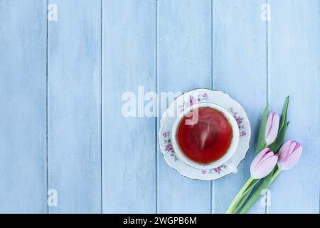 Dampfender heißer Tee und rosafarbene Tulpenblüten über einem rustikalen blauen Holztisch. Ansicht der Tischaufsicht. Direkt darüber. Stockfoto