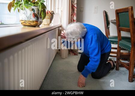 Ältere Frau, die den Heizungssensor am Heizkörper überprüft Stockfoto