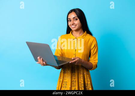 Glückliche Dame aus dem Nahen Osten, die einen Laptop vor blauem Hintergrund benutzt Stockfoto