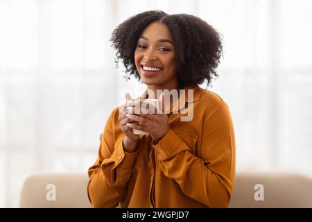 Eine strahlende junge Frau mit üppigen lockigen Haaren, gekleidet in einer senfeinfarbenen Bluse Stockfoto