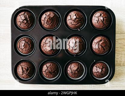 Über dem Blick auf kleine gebackene Schokoladenmuffins in der Muffinpfanne drinnen im Haus auf Holzhintergrund. Kreativer Hintergrund. Stockfoto