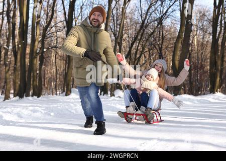 Glückliche Familie, die Spaß mit Schlitten im verschneiten Wald hat Stockfoto