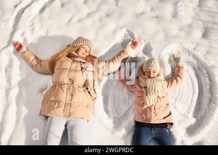 Familienzeit. Glückliche Mutter und ihre Tochter machen Schneeengel am sonnigen Wintertag, über der Aussicht Stockfoto