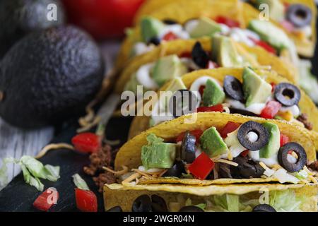 Tacos aus Maistortillas, gemahlenem Rindfleisch, geriebenem Cheddar, schwarzen Oliven, Avocados, Salat, Sauerrahm und Tomaten. Selektiver Fokus. Stockfoto