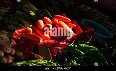 Eine lebhafte Auswahl an roten Karotten und anderem frischem Gemüse, das auf einem Bauernmarkt präsentiert wird Stockfoto