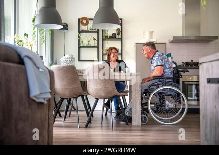 Die Frau bereitet ihr Mittagessen vor, der in seinem Rollstuhl am Tisch sitzt Stockfoto