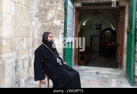 Hof der Grabeskirche, koptischer Mönch, der vor der Tür der koptischen Kirche in Jerusalem sitzt Stockfoto