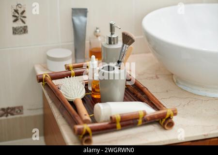 Set mit Selbstliebe-Artikeln in Bambustablett, die oben auf dem Schrank mit weißem Porzellanwaschbecken im Badezimmer eines modernen Apartments stehen Stockfoto