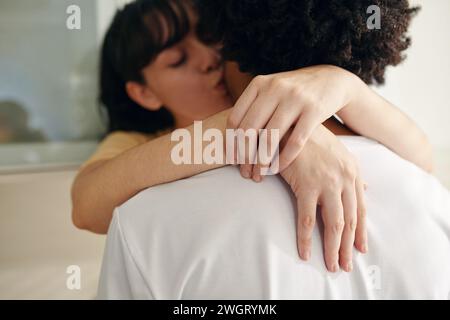 Hände einer jungen zärtlichen Frau mit geschlossenen Augen, die ihren Mann am Hals umarmen und ihn vor der Kamera küssen Stockfoto