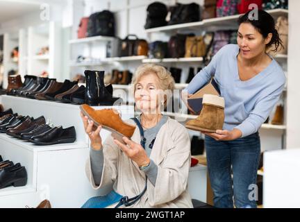 Freundliche weibliche Verkaufsberaterin bedient eine reife Frau, die sich Schuhe anprobieren wird Stockfoto