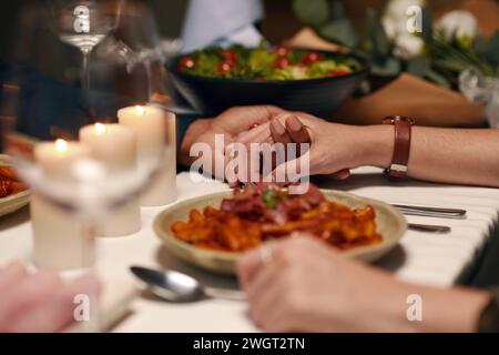 Hände junger interkultureller liebevoller Valentinskinder, die am Tisch vor der Kamera sitzen und ein festliches Abendessen zu Hause oder im Restaurant genießen Stockfoto