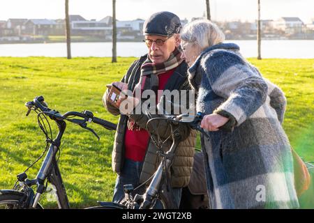 Ältere Paare, die eine Radtour machen, um fit und gesund in ihrem Ruhestand zu bleiben. Verwenden des Telefons, um nach Hause zu navigieren Stockfoto