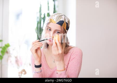 Eine junge Frau mit blondem Haar schminkt sich mit einem Ei Stockfoto