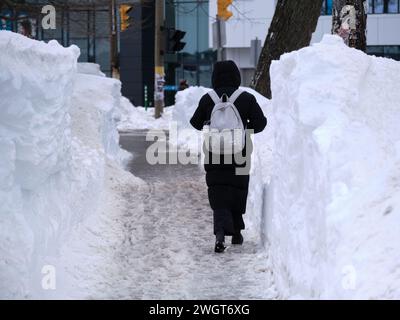 Halifax, Nova Scotia, Kanada. Februar 2024. Nach dem größten Schneesturm seit 20 Jahren in Halifax ist der Aufräumprozess im Gange. Fußgänger auf Bell Road Gehwegen mit über einen Meter hohen Schneebänken auf jeder Seite Credit: Meanderingemu/Alamy Live News Stockfoto