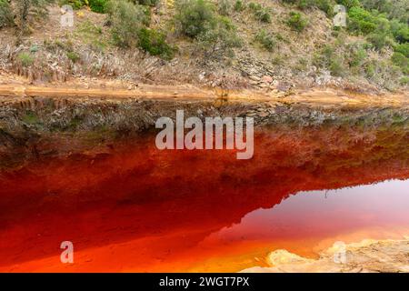 Markante Erdschichten und ein lebhafter Streifen rotes Wasser säumen den zerrissenen Boden des Rio Tinto Stockfoto