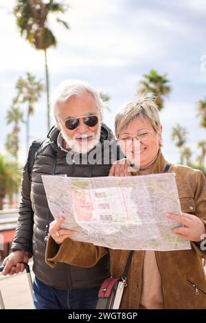 Älteres kaukasisches Touristenpaar lächelt mit Reisekarte in der Hand und sucht zusammen interessante Orte. Stockfoto