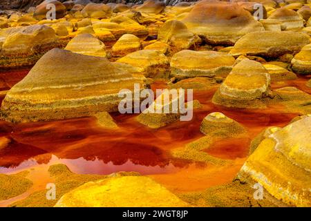 Geschichtete, eisenbeschichtete Steine tauchen aus dem rötlichen, sauren Wasser in der einzigartigen Landschaft von Rio Tinto auf Stockfoto