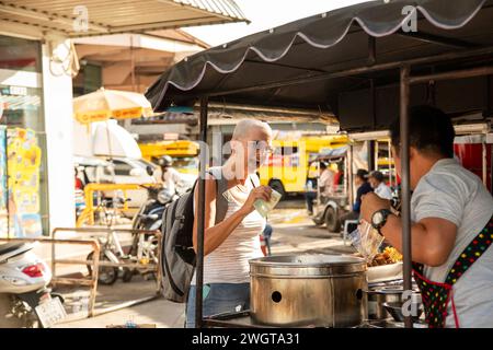 Alleinreisender mittleren Alters hält an, um Straßenessen von einem Händler in Chiang Mai zu kaufen. Thailand Stockfoto