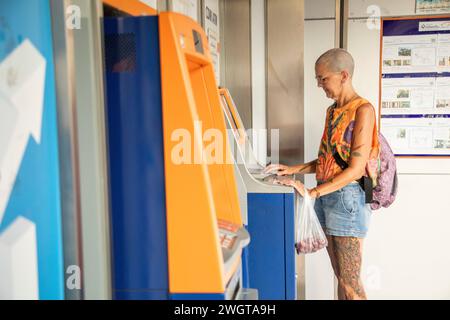 Frau mittleren Alters Alleinreisender, hält am Geldautomaten, um lokale Währung abzuheben, sie sieht ernst aus. Stockfoto