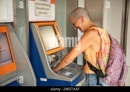 Frau mittleren Alters Alleinreisender, hält am Geldautomaten, um lokale Währung abzuheben, sie sieht glücklich aus. Stockfoto
