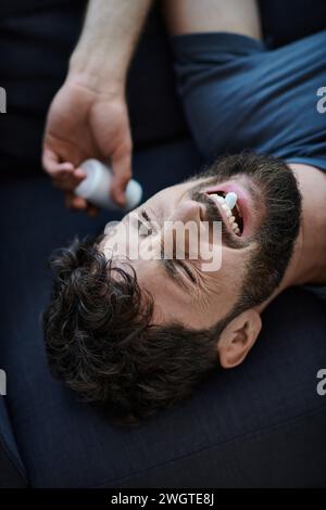 Emotional depressiver Mann mit Bart, der Pillen während depressiver Episode nimmt, geistiges Gesundheitsbewusstsein Stockfoto