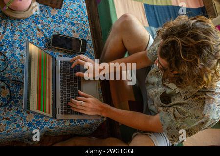 Der junge Mann arbeitet an seinem Laptop und Handy in einem Restaurant in Nordthailand, er ist ein digitaler Nomad, der aus der Ferne arbeitet. Stockfoto