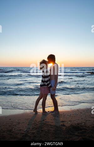 Silhouetten eines küssenden jungen Paares vor dem Hintergrund des Meeres und Sonnenuntergangs, ein Mann und ein verliebtes Mädchen zusammen im Urlaub. Genießen Sie den Moment, Stockfoto