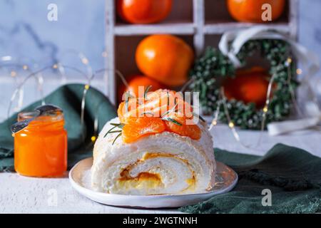 Meringue-Rolle gefüllt mit Mascarpone, Creme und Mandarinenmarmelade auf einem Hintergrund von Mandarinen und einem grünen Herzen. Stockfoto