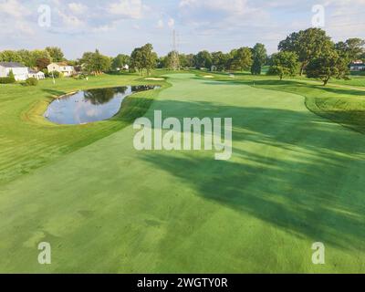 Blick aus der Vogelperspektive auf den ruhigen Vorort-Golfplatz mit Wassergefahr und reiferen Bäumen Stockfoto