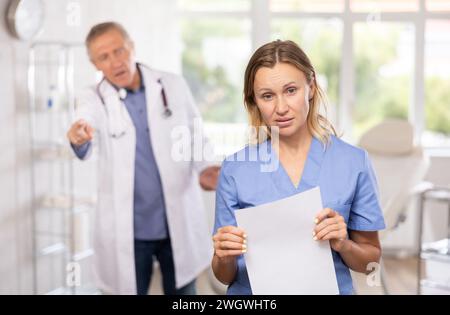 Verärgerte Krankenschwester mittleren Alters, die mit dem Rücken zum wütenden Arzt stand Stockfoto