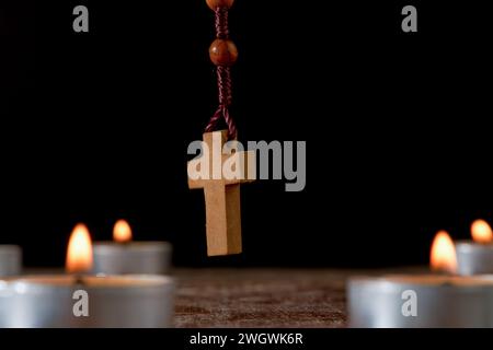 Kreis aus beleuchteten Kerzen mit einem hölzernen Rosenkranz betenden Perlen in der Mitte und einem schwelenden Weihrauch im Hintergrund isoliert auf schwarzem Hintergrund Stockfoto