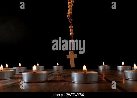 Kreis aus beleuchteten Kerzen mit einem hölzernen Rosenkranz betenden Perlen in der Mitte und einem schwelenden Weihrauch im Hintergrund isoliert auf schwarzem Hintergrund Stockfoto
