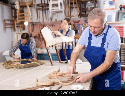 Senior männlicher Möbelhersteller, der in der Werkstatt an Vintage-Stuhlteilen arbeitet Stockfoto